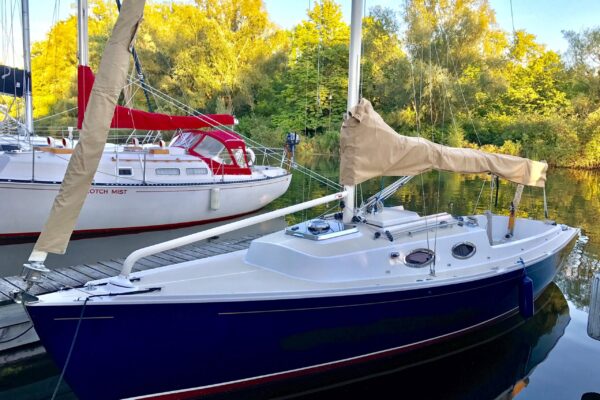 2010 Schock Harbor 25 sailboat docked, surrounded by lush greenery and calm waters.